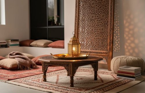 Moroccan-inspired living room corner with a low tea table, layered textiles, carved mashrabiya shadow patterns, and a warm metal lantern glow.