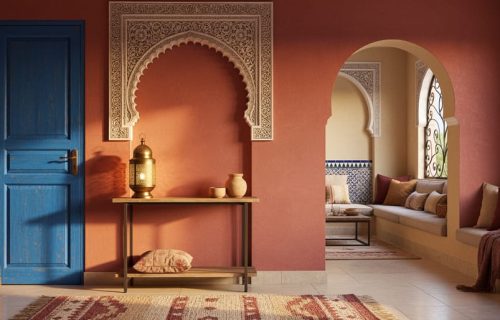 Moroccan-inspired interior with a deep terracotta/red accent wall, ornate archway details, and cobalt blue accents in warm golden light.