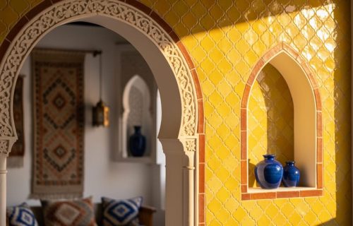 Close-up of sunlit yellow Moroccan zellige tiles in a Moroccan riad interior with arched architectural details and softly blurred blue decor in the background.